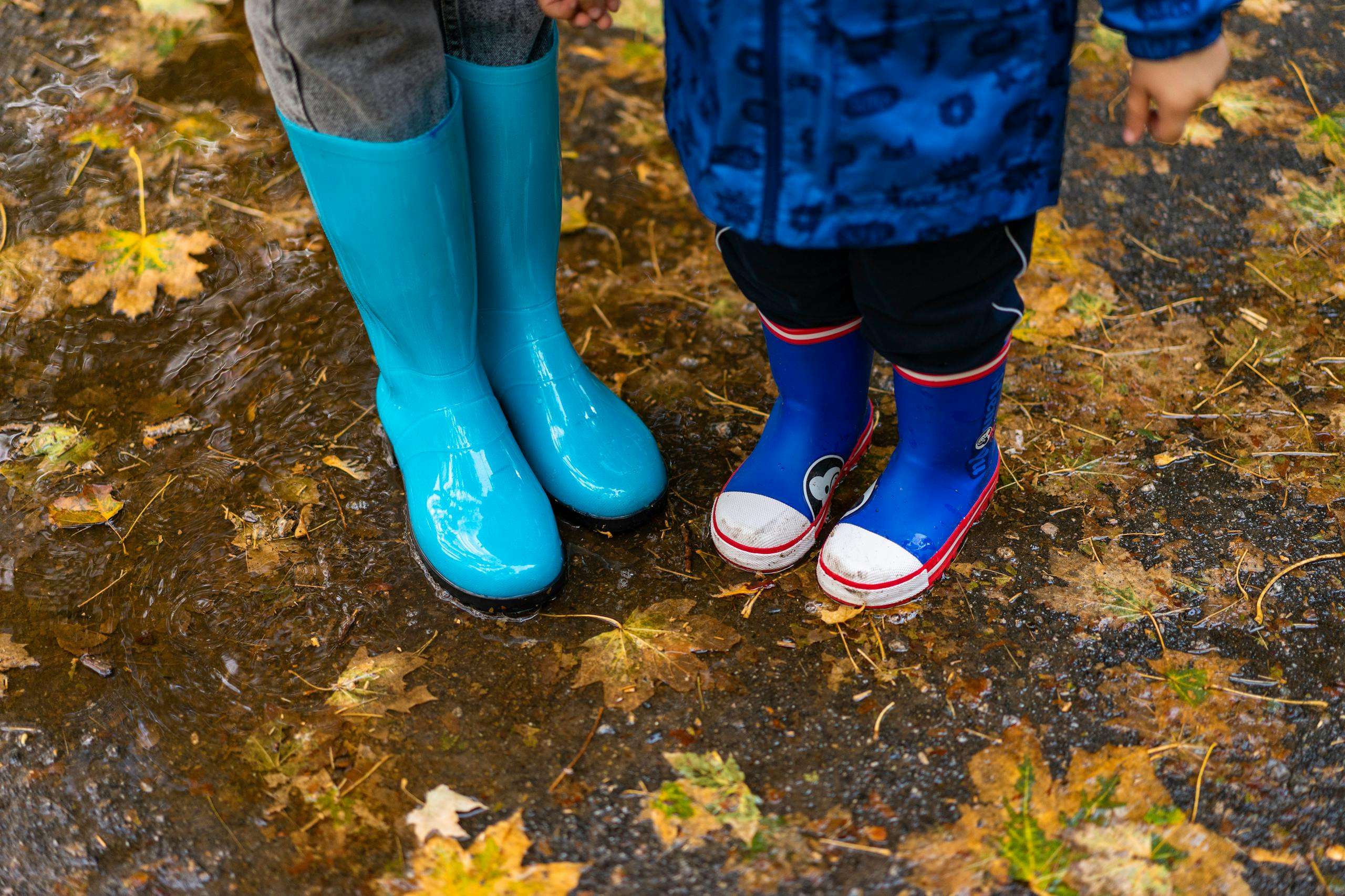 Two children wearing bright rubber boots splash in autumn puddles covered with fallen leaves. fun activities for kids on rainy days