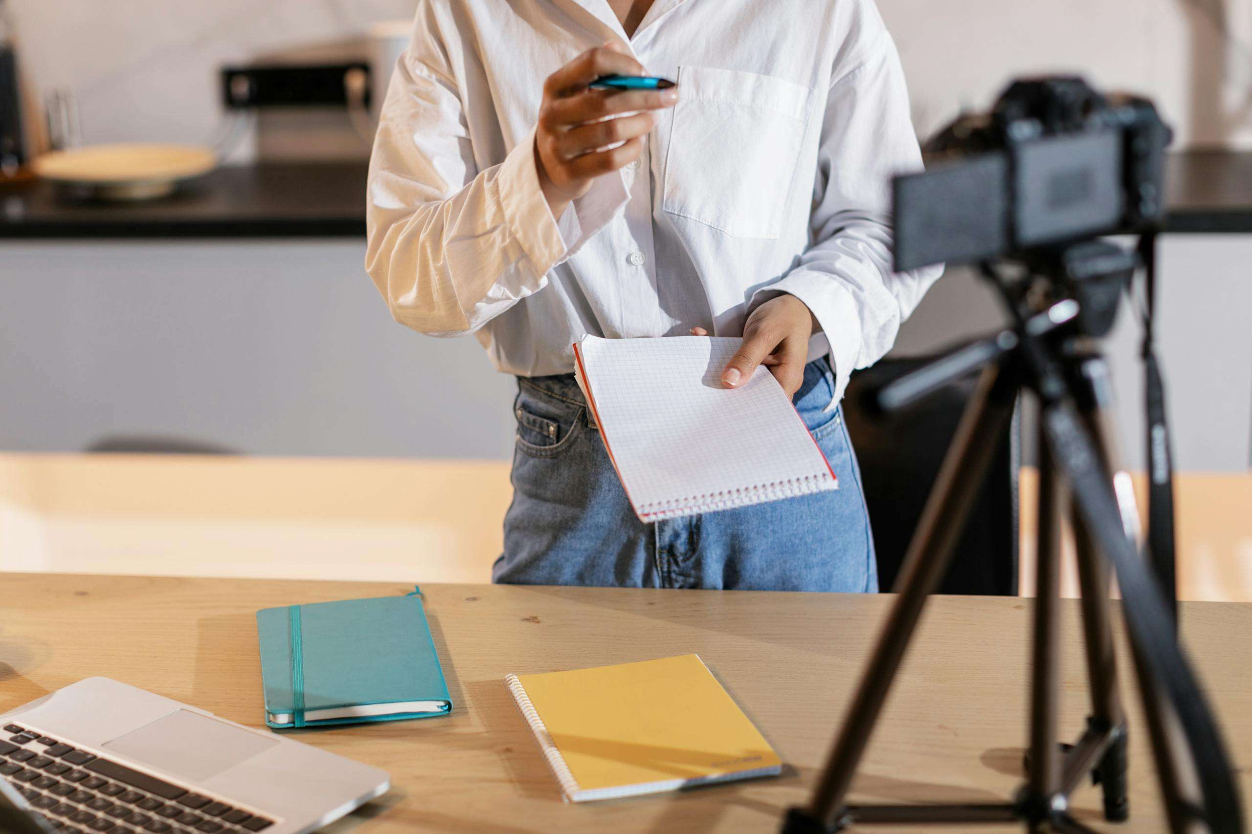 Vlogger recording content with a camera, holding notes and using a laptop in a modern setting. content creation tips to stand out online