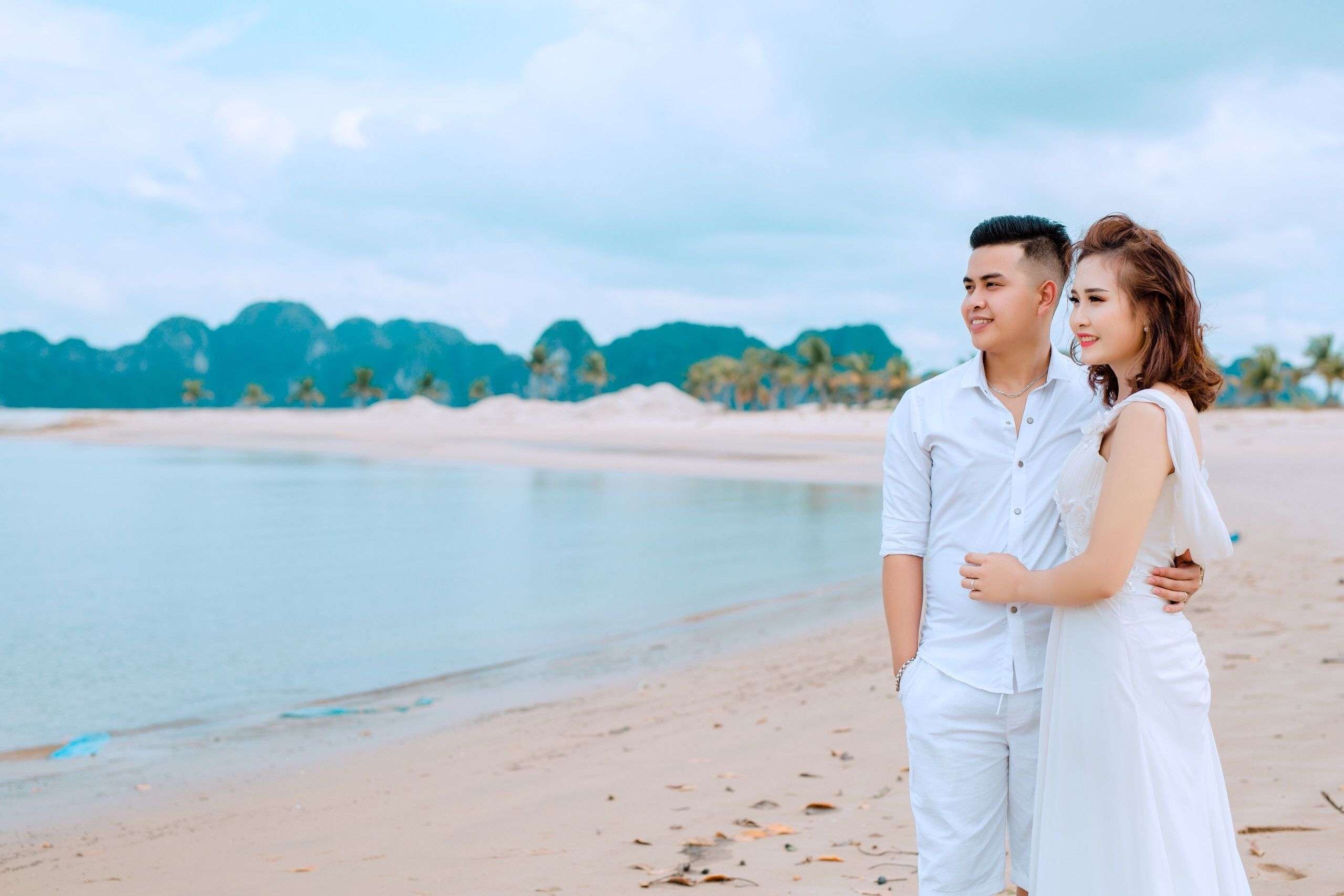 Young couple in white attire embracing on a serene tropical beach at sunrise. Perfect for romance and travel themes.